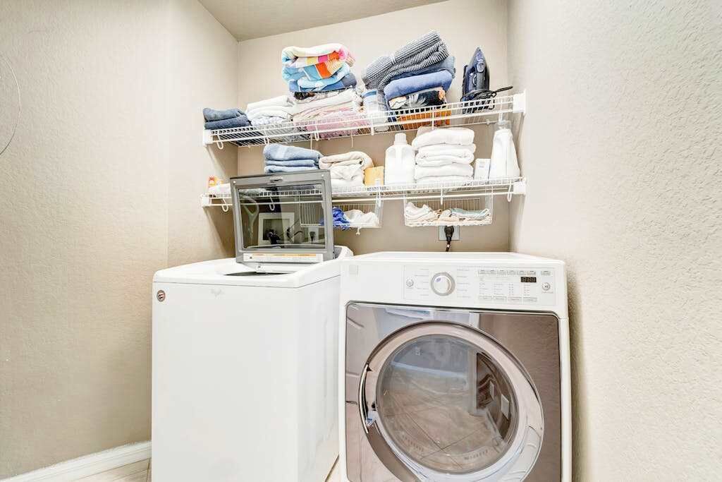Un espace buanderie comprenant un lave-linge et un sèche-linge, des étagères avec des vêtements pliés et une petite étagère avec des articles de toilette.