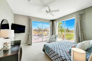 A bedroom with a bed, a TV, a ceiling fan, a balcony with a chair, and a view of the outdoors. - Luxe waterfront townhome with water views, 4 decks, & all-new interior (Englewood)