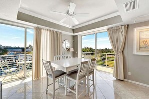 A dining area with a white table and chairs, a ceiling fan, and large windows with curtains. - Luxe waterfront townhome with water views, 4 decks, & all-new interior (Englewood)