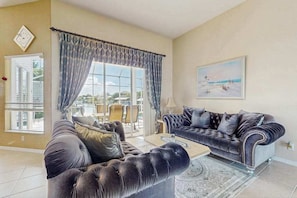 A living room with a large window, a sofa, a coffee table, and a painting on the wall. - Dog friendly home with private pool, washer & dryer, and Wifi (Marco Island)
