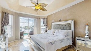 Ein Schlafzimmer mit Bett, Deckenventilator, Nachttisch und Blick durch das Fenster.