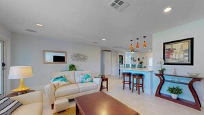 A modern living room with a sofa, coffee table, and a kitchen area with bar stools. - Elegant dog-friendly all-suite boater’s paradise near beach with private dock (Naples)