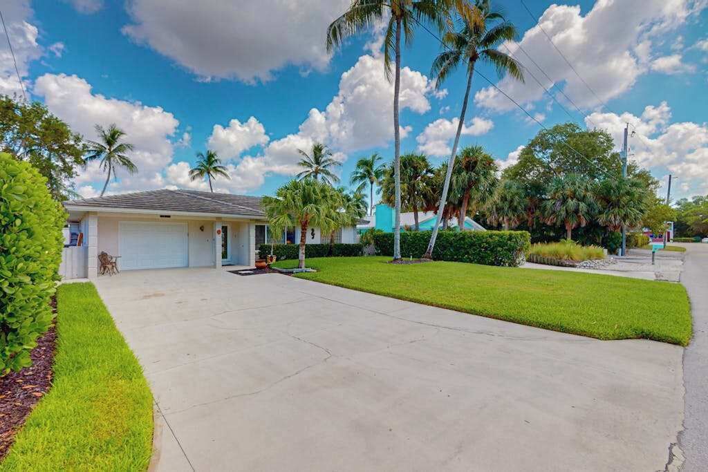 A residential property with a well-maintained lawn, a garage, and palm trees.