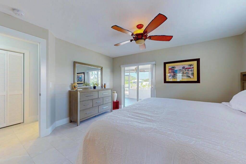 A bedroom with a bed, a dresser, a ceiling fan, a window, and a door.