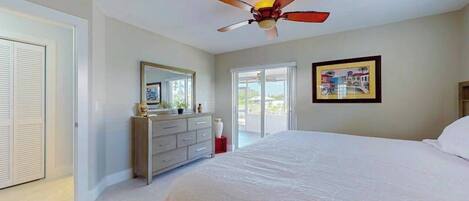 A bedroom with a bed, a dresser, a ceiling fan, a window, and a door.