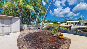 A pool area with a pebble ground, palm trees, and a building with a garage. - Elegant dog-friendly all-suite boater’s paradise near beach with private dock (Naples)