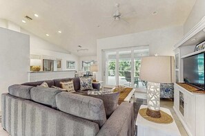 A modern living room with a grey sofa, a television, and a ceiling fan. - Coastal home with private, heating optional pool, lanai, and internet (Marco Island)