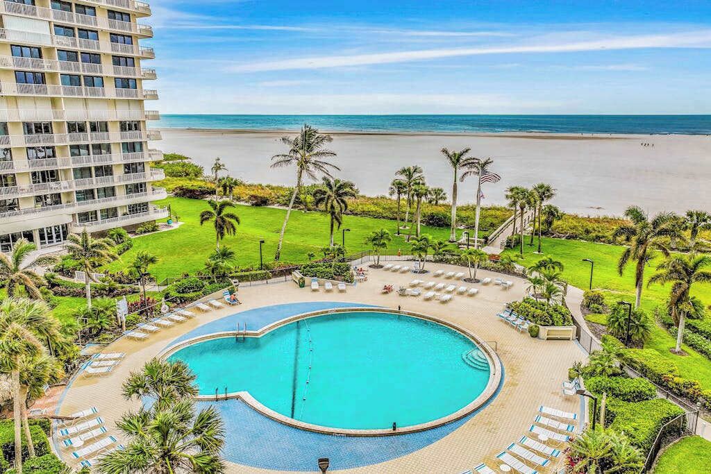 A hotel with a pool, beach view, and palm trees.