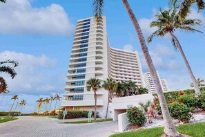 Ein mehrgeschossiges Hotel mit einer geschwungenen Fassade, Palmen und einer gepflasterten Auffahrt.