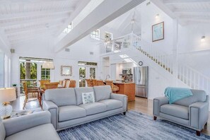 Ein geräumiger Wohnbereich mit hoher Decke, einer Treppe und einer Küche im Hintergrund.