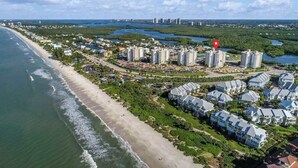 Eine Vogelperspektive auf eine Küstenwohngegend mit Immobilien direkt am Strand, einem Yachthafen und einer dichten Ansammlung von Hochhäusern im Hintergrund.