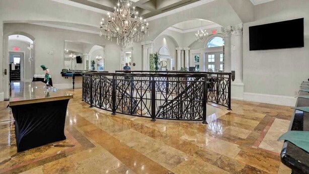 Um hall amplo com piso de mármore, um lustre central e uma mesa de recepção.