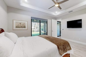 A bedroom with a bed, a ceiling fan, a TV, and a sliding glass door leading to an outdoor area.