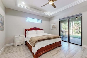 A bedroom with a bed, a nightstand, a ceiling fan, a window, and a sliding glass door leading to an outdoor area.