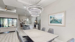 A modern kitchen with white cabinets, a dining area with a marble table, and a large window providing a view of the outdoors. - Luxurious home with private washer/dryer, enclosed yard, WiFi, & screened lanai (Bonita Springs)