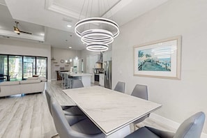 A modern kitchen with white cabinets, a dining area with a marble table, and a large window providing a view of the outdoors.