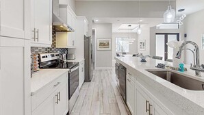A modern kitchen with white cabinetry, stainless steel appliances, and a large island with a sink. - Luxurious home with private washer/dryer, enclosed yard, WiFi, & screened lanai (Bonita Springs)