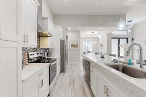 A modern kitchen with white cabinetry, stainless steel appliances, and a large island with a sink.