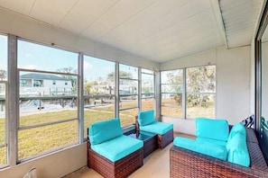 A sunroom with large windows, wicker furniture, and a view of the outdoors. - Canal front apartment with waterfront views, private patio, and yard (Bonita Springs)