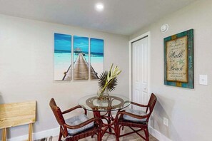 A dining area with a glass table, wicker chairs, and a tropical plant centerpiece. - Canal front apartment with waterfront views, private patio, and yard (Bonita Springs)
