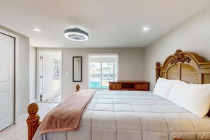 A bedroom with a bed, bedside tables, a wooden headboard, a window with blinds, and a ceiling light. - Canal front apartment with waterfront views, private patio, and yard (Bonita Springs)