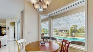 Un comedor con una mesa, sillas, una lámpara de araña y un ventanal con vistas a una piscina.