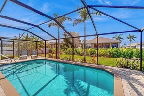 Une piscine dotée d’une enceinte en verre, entourée de palmiers et avec une maison en arrière-plan.