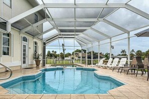 A covered swimming pool with lounge chairs and a view of the surrounding landscape. - Villa Euphoria: Chic 2-unit, canal-front retreat with 2 pools & private dock (Cape Coral)