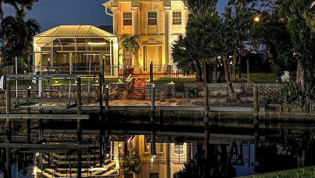 A waterfront property with a large house, a covered patio, and a dock. - Villa Euphoria: Chic 2-unit, canal-front retreat with 2 pools & private dock (Cape Coral)