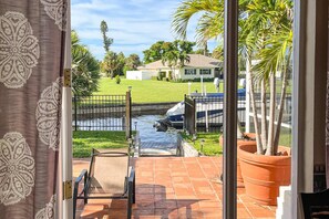 A patio with a chair, a view of a house across a water body, and a large potted plant. - Villa Euphoria: Chic 2-unit, canal-front retreat with 2 pools & private dock (Cape Coral)