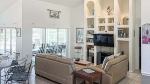 A living room with a sofa, a TV, and a bookshelf. - Villa Euphoria: Chic 2-unit, canal-front retreat with 2 pools & private dock (Cape Coral)
