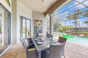 Eine Außenpatio mit einem Glastisch und Stühlen, einem Swimmingpool und Palmen im Hintergrund.