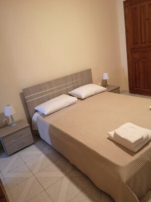 A hotel room with a large bed, two bedside tables with lamps, a wooden wardrobe, and a tiled floor. - Village View Nea Epidavros (Nea Epidavros)