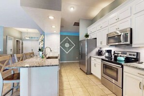 A modern kitchen with granite countertops, stainless steel appliances, and a central island. - Luxury coastal retreat with office, lanai, pool, alfresco dining & tiki bar (Cape Coral)