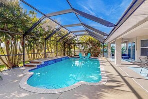 A swimming pool with a glass enclosure, surrounded by palm trees and a covered patio area. - Luxury coastal retreat with office, lanai, pool, alfresco dining & tiki bar (Cape Coral)