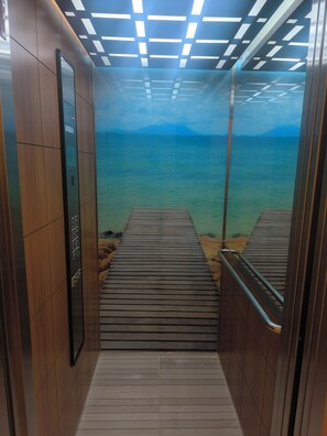 Ein Aufzug mit Blick auf ein Holzdeck, das zu einem Gewässer führt, mit einem Berg im Hintergrund.