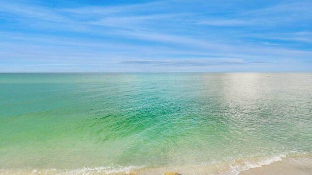 En strand med krystalklart turkis vand og en blå himmel.