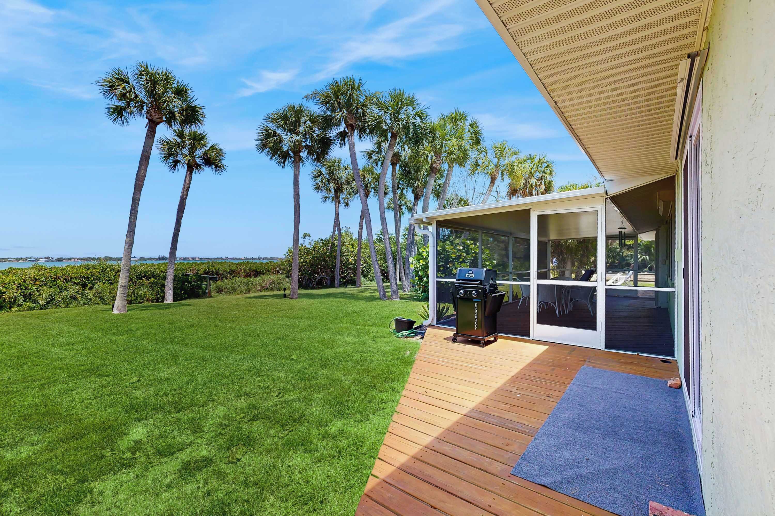 Un patio con una parrilla, una terraza de madera y vistas a palmeras.