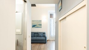 Um corredor leva a um quarto com um sofá azul, um quadro na parede e uma porta com um porta-toalhas.