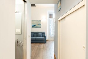 Ein Flur, der zu einem Raum mit einem blauen Sofa, einem Gemälde an der Wand und einer Tür mit Handtuchhalter führt.