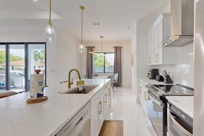 A modern kitchen with a central island, stainless steel appliances, and pendant lighting. - New modern home with pool, lawn, W/D, Wifi and AC (Cape Coral)
