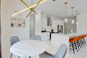 A modern kitchen with white cabinets, a central island with bar stools, and pendant lighting. - New modern home with pool, lawn, W/D, Wifi and AC (Cape Coral)