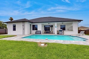 A modern two-story house with a swimming pool, a patio with outdoor furniture, and a covered area with a grill. - New modern home with pool, lawn, W/D, Wifi and AC (Cape Coral)