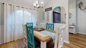 Un coin repas avec une table en bois, des chaises de couleur turquoise, des rideaux blancs et un lustre.