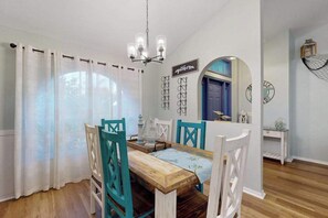 Un coin repas avec une table en bois, des chaises de couleur turquoise, des rideaux blancs et un lustre.