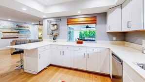 Una cocina moderna con armarios blancos, un taburete de bar, una ventana con vistas y un ventilador de techo.