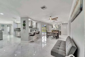 A spacious living area with a sofa, a dining table, and a kitchen in the background. - Dog-friendly water-view house with pool & firepit - snowbirds welcome (Cape Coral)