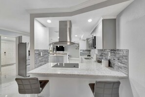 A modern kitchen with a central island, stainless steel appliances, and a marble backsplash. - Dog-friendly water-view house with pool & firepit - snowbirds welcome (Cape Coral)