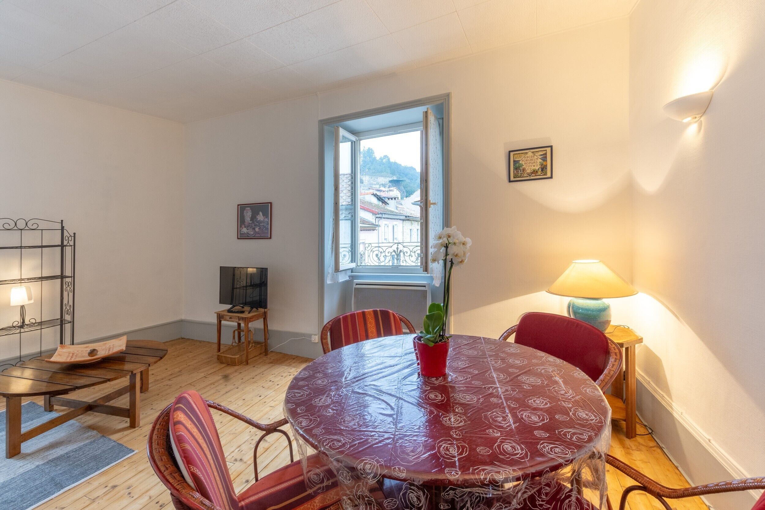 Een kamer met een ronde tafel, stoelen, een televisie, een raam en een lamp.