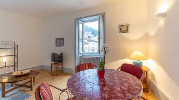 Een kamer met een ronde tafel, stoelen, een televisie, een raam en een lamp.